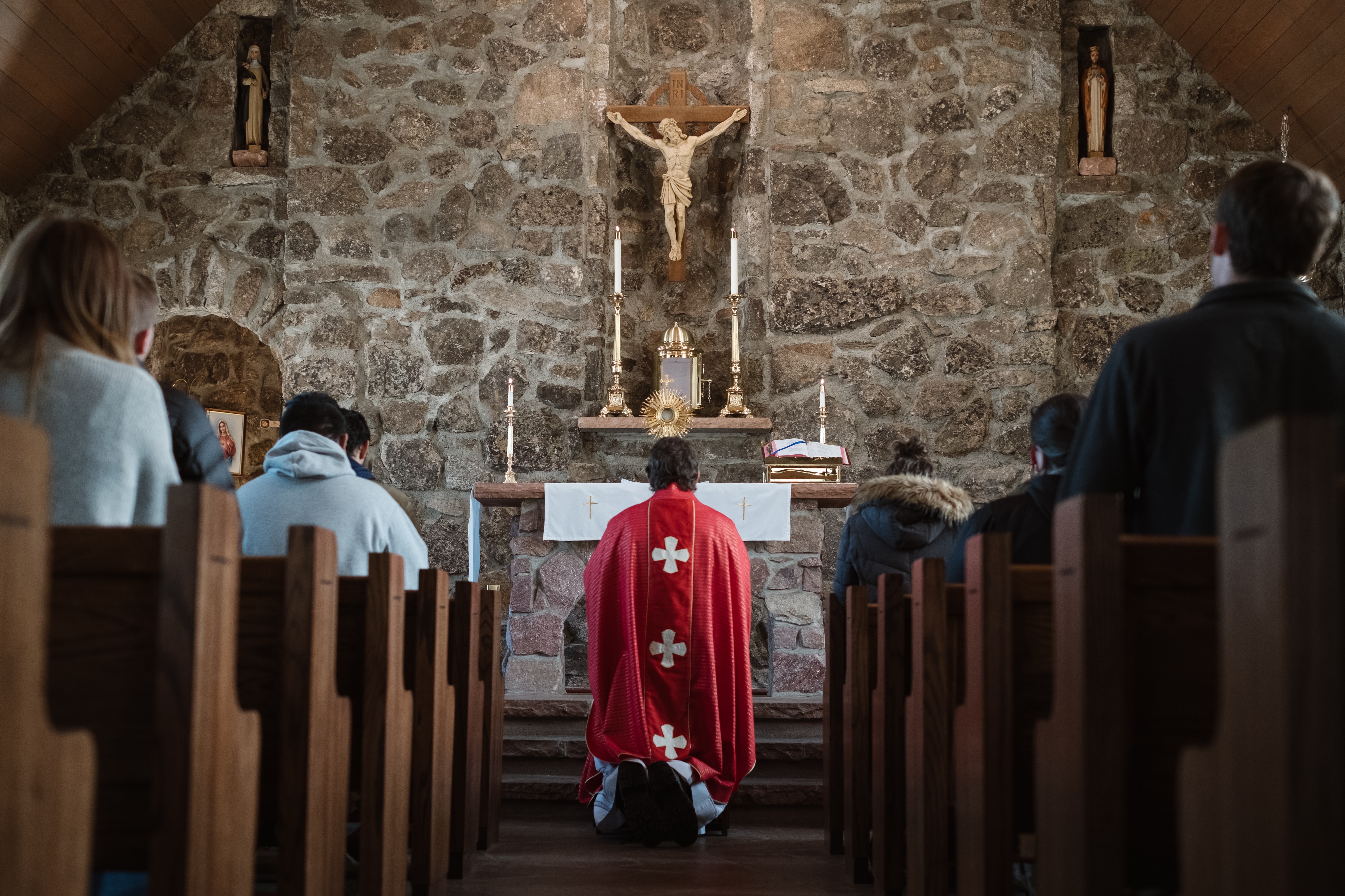 A member of the clergy kneeling at the front of a church as people sitting in the pews look on